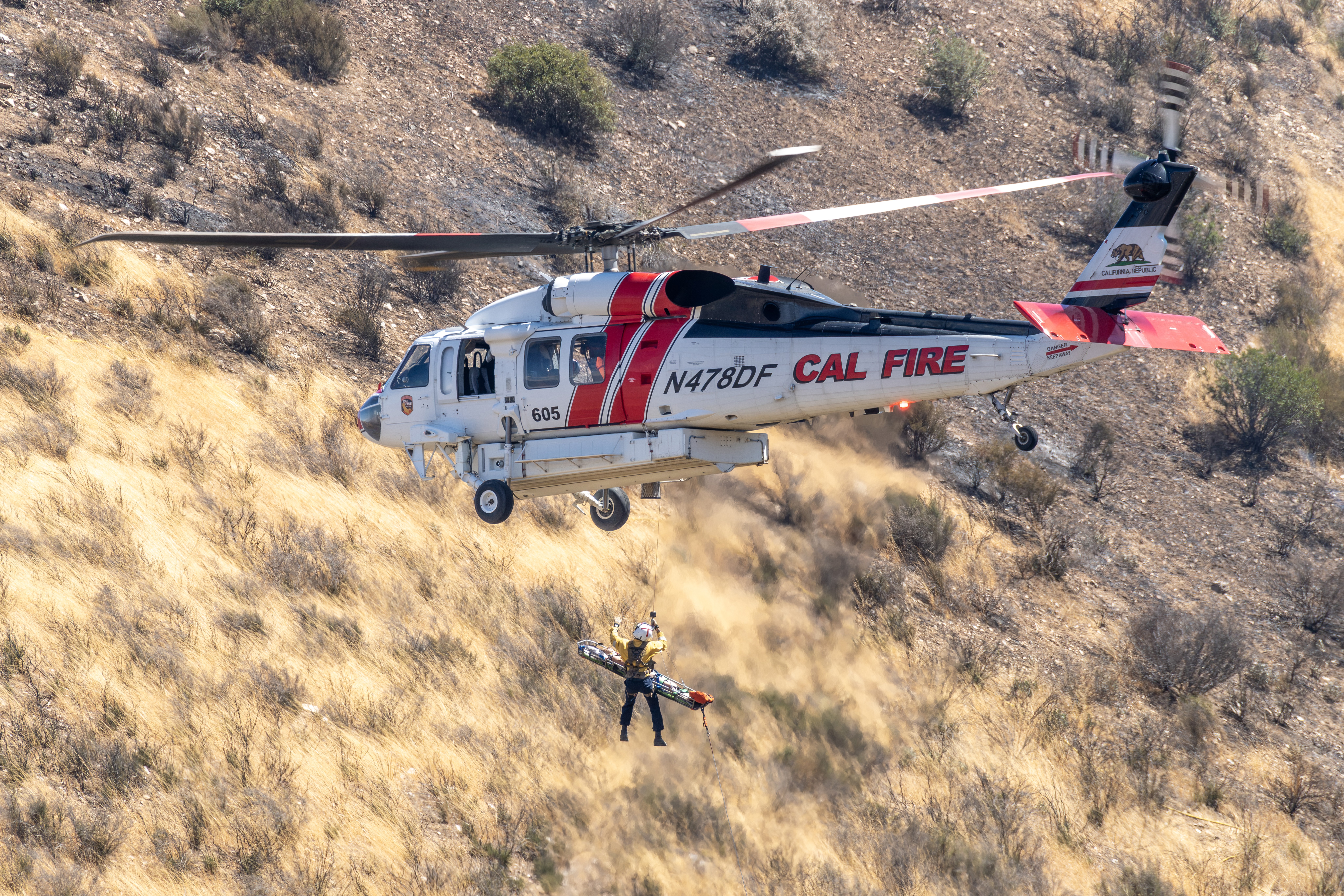 This is a real rescue at the Panorama Fire off of the mountain Highway 243 above Banning , California which was caused by a young woman going over the side in her vehicle and it catching on fire. This is a story of a true hero. People on the road above heard the young women screaming for help and a man climbed down the steep embankment about 200 feet down.The fire was burning all around them and he only had seconds to get her to a safe place. She was going in and out of consciousness and so he decided to cary her on his back. He couldn't climb back up the steep embankment, so he hiked down the hill away from the flames. As you can see from this picture, she was airlifted out and taken to a hospital. She sustained multiple injuries, some requiring surgery.