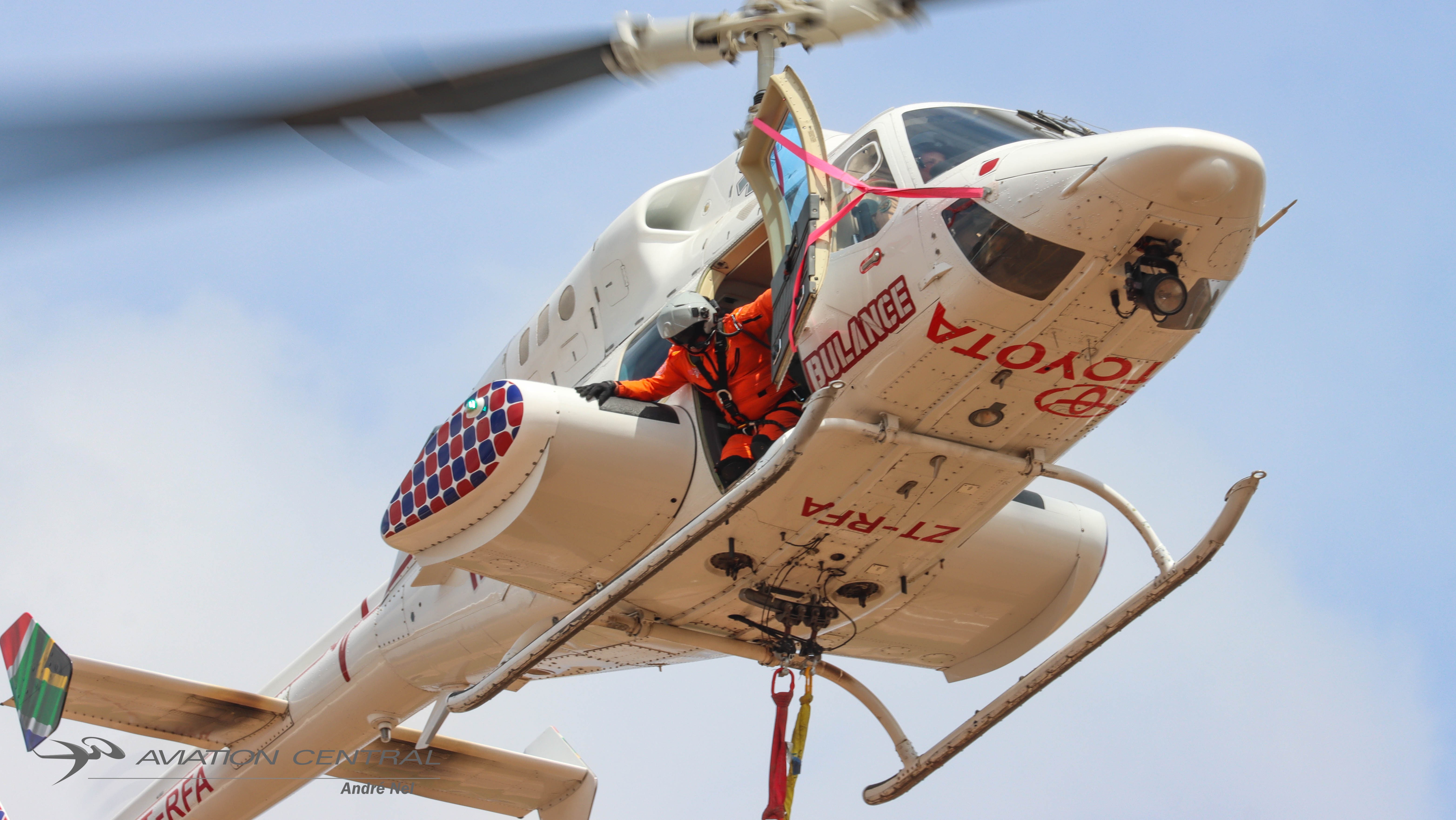 Henley Air Bell 222UT ZT-RFA during the flying display at Africa Aerospace and Defence 2026 at AFB Waterkloof, South Africa. A crew member works from the open cabin door as the helicopter performs its demonstration.