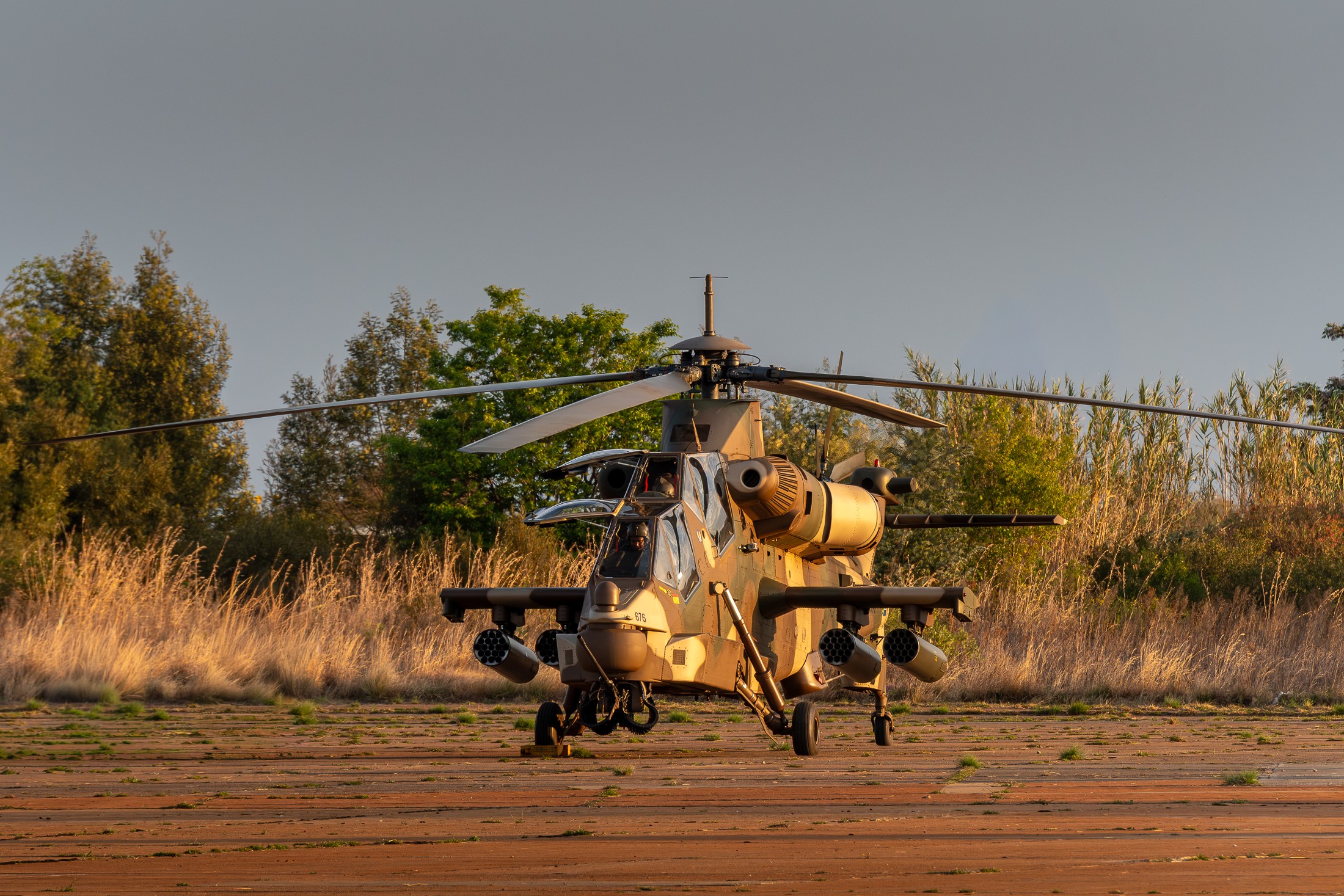A South African Air Force Denel AH-2 Rooivalk sits in the late-afternoon light at AFB Waterkloof following its final flying display at Africa Aerospace and Defence 2026. With the canopy still open and the aircraft illuminated by the setting sun, the image captures a quiet moment immediately after the noise and intensity of the display.