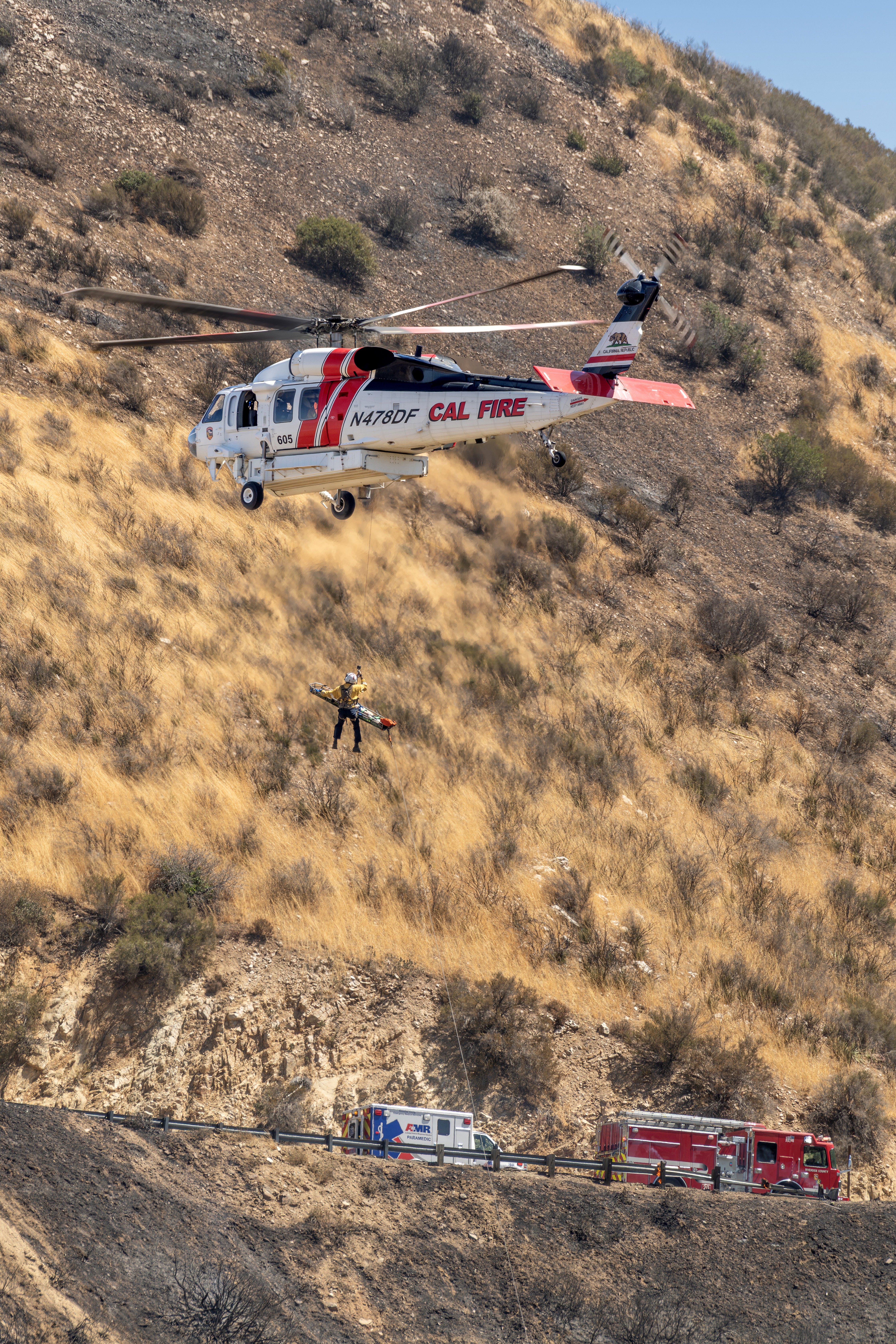 This is a real rescue at the Panorama Fire off of the mountain Highway 243 above Banning, California which was caused by a young woman going over the side in her vehicle and it catching on fire. This is a story of a true hero. People on the road above heard the young women screaming for help and a man climbed down the steep embankment about 200 feet down. The fire was burning all around them and he only had seconds to get her to a safe place. She was going in and out of consciousness and so he decided to carry her on his back. He couldn't climb back up the steep embankment, so he hiked down the hill away from the flames. As you can see from this picture, she was airlifted out and taken to a hospital. She sustained multiple injuries, some requiring surgery.