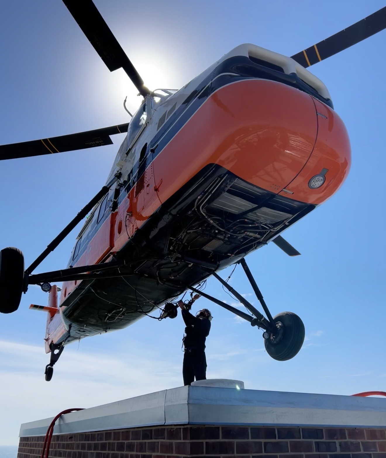 A Midwest Helicopter Airways Sikorsky S-58T hovers just feet above a rooftop as a crew member connects the aircraft’s external-load rigging for the next lift. Captured from the rooftop, the photo shows just how close the teamwork gets during aerial crane operations. With the aircraft holding steady overhead, the ground crew and pilot work together to safely and efficiently keep the job moving—one lift at a time.