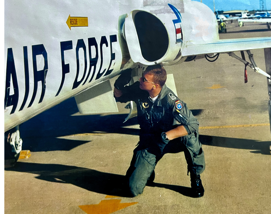 A man in a military uniform is kneeling down next to a jet engine. AI generated content