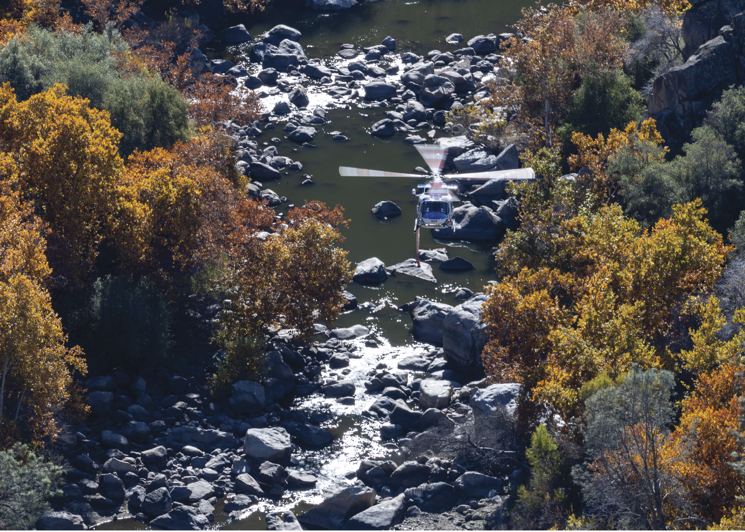 A helicopter is flying over a river with rocks in the water. AI generated content