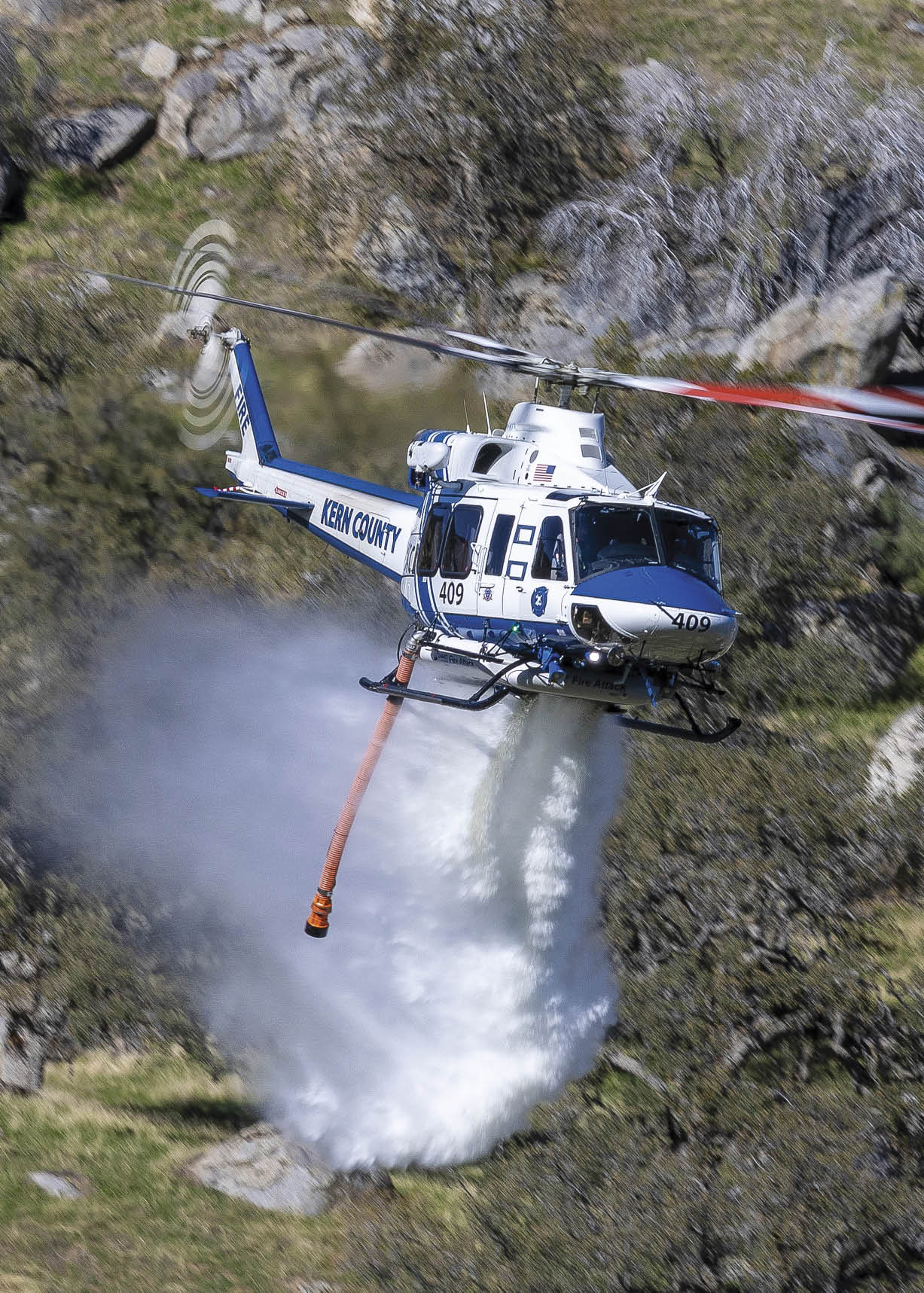 A blue and white helicopter is flying over a rocky hillside, spraying water onto the ground. AI generated content