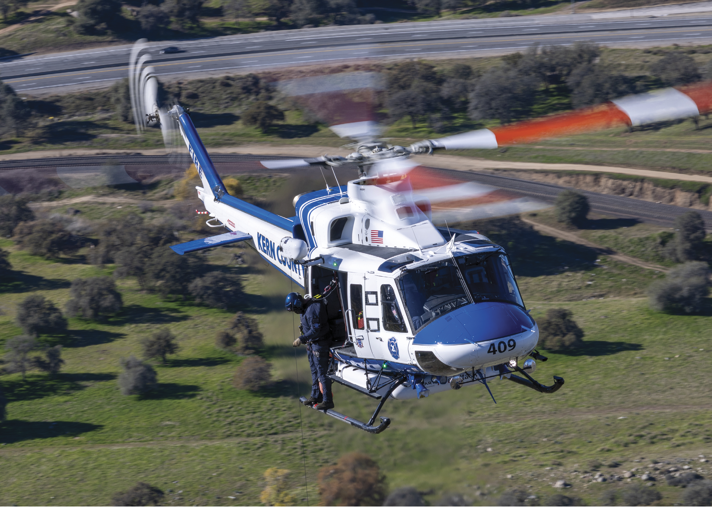 A blue and white helicopter is flying over a grassy field. AI generated content
