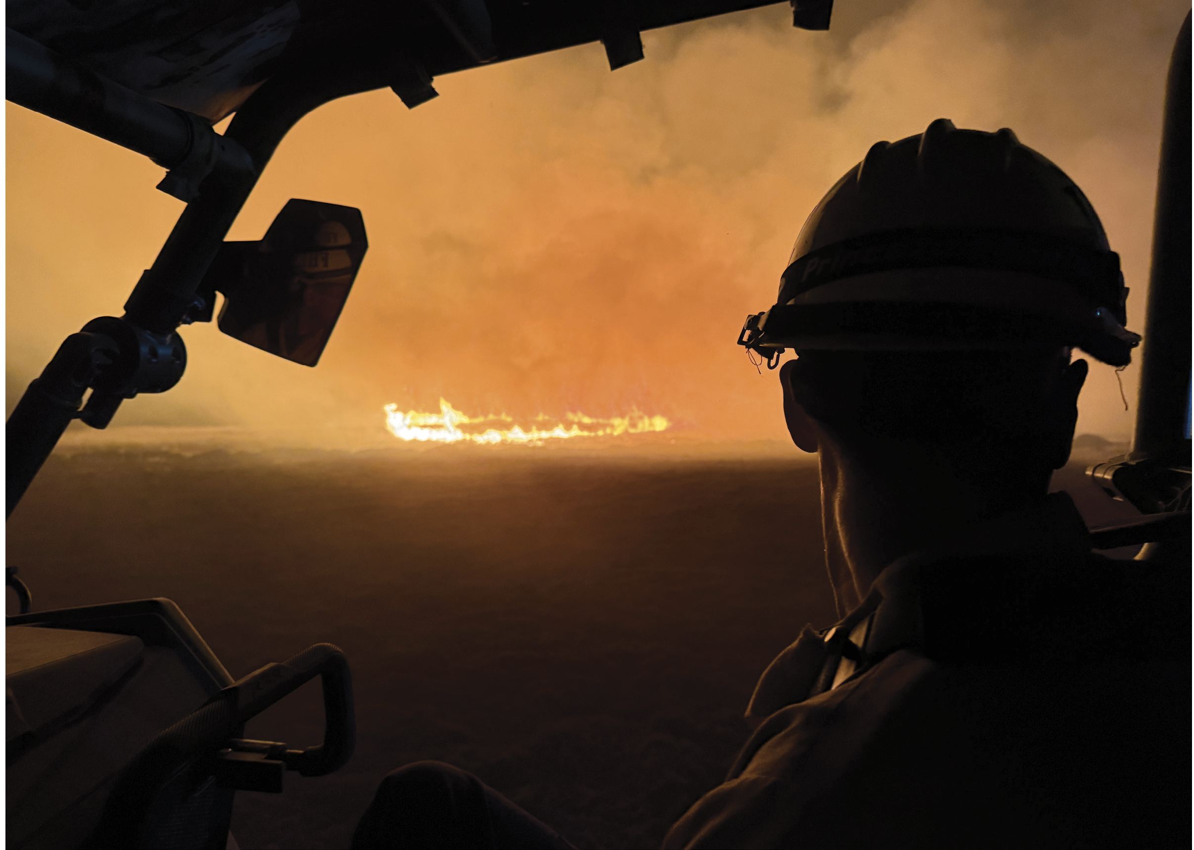 A man wearing a helmet is sitting in a helicopter, looking at a fire in the distance. AI generated content