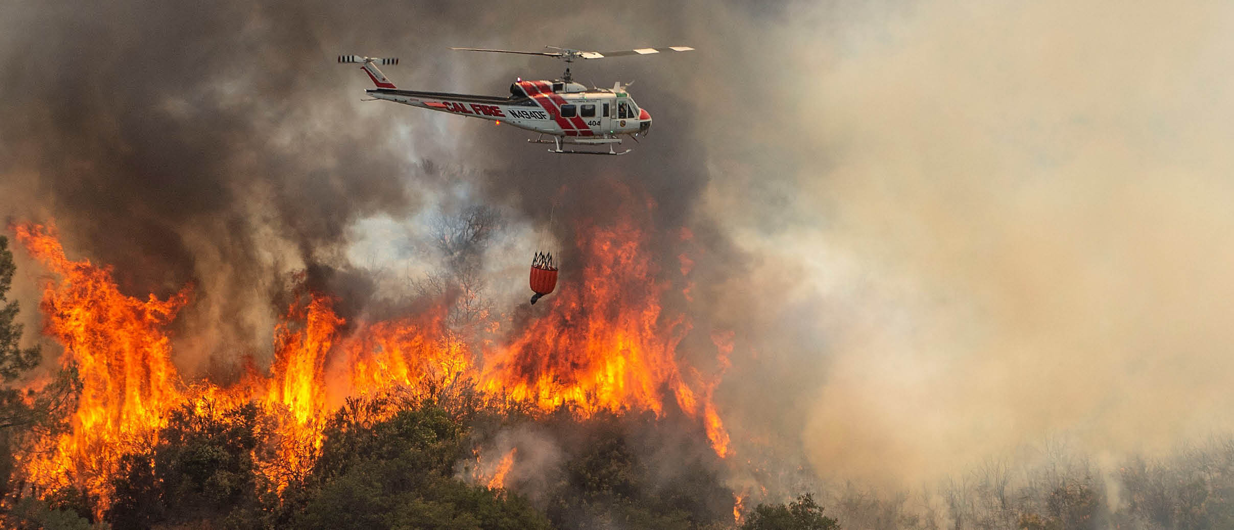 A helicopter is flying over a forest fire, dropping water to extinguish the flames. AI generated content