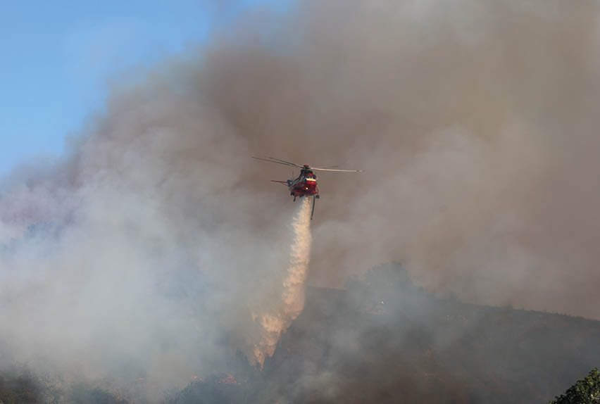 A red helicopter is flying over a forest, spraying water to extinguish a fire. AI generated content