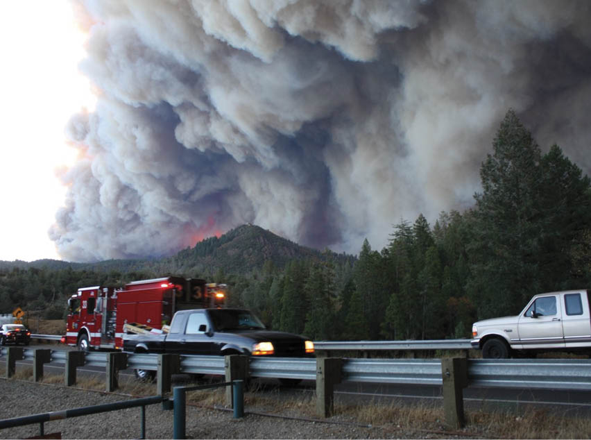 A fire truck is parked on the side of a road, with a large fire in the distance. AI generated content