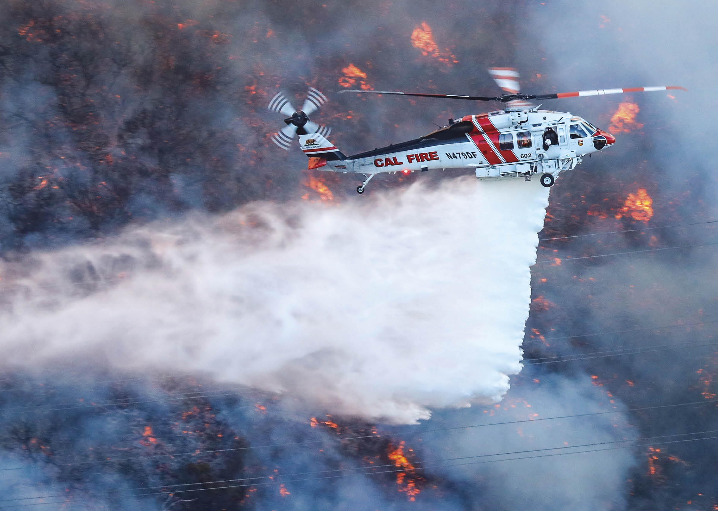 A helicopter is flying over a forest fire, spraying water to extinguish the flames. AI generated content