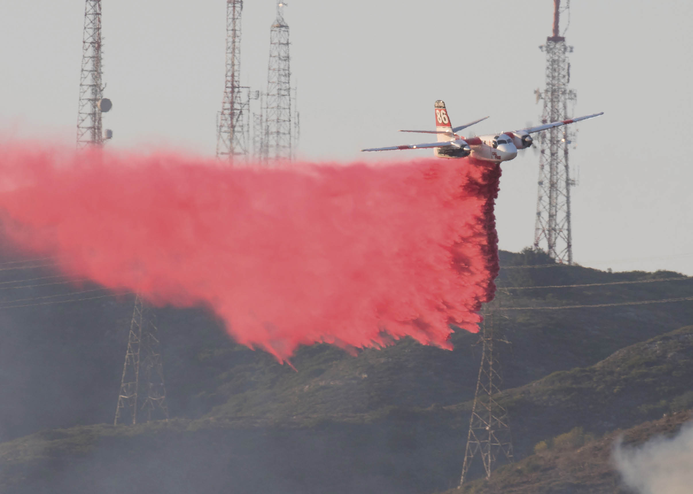 A plane is flying over a hillside with a red trail behind it, possibly from a fire. AI generated content