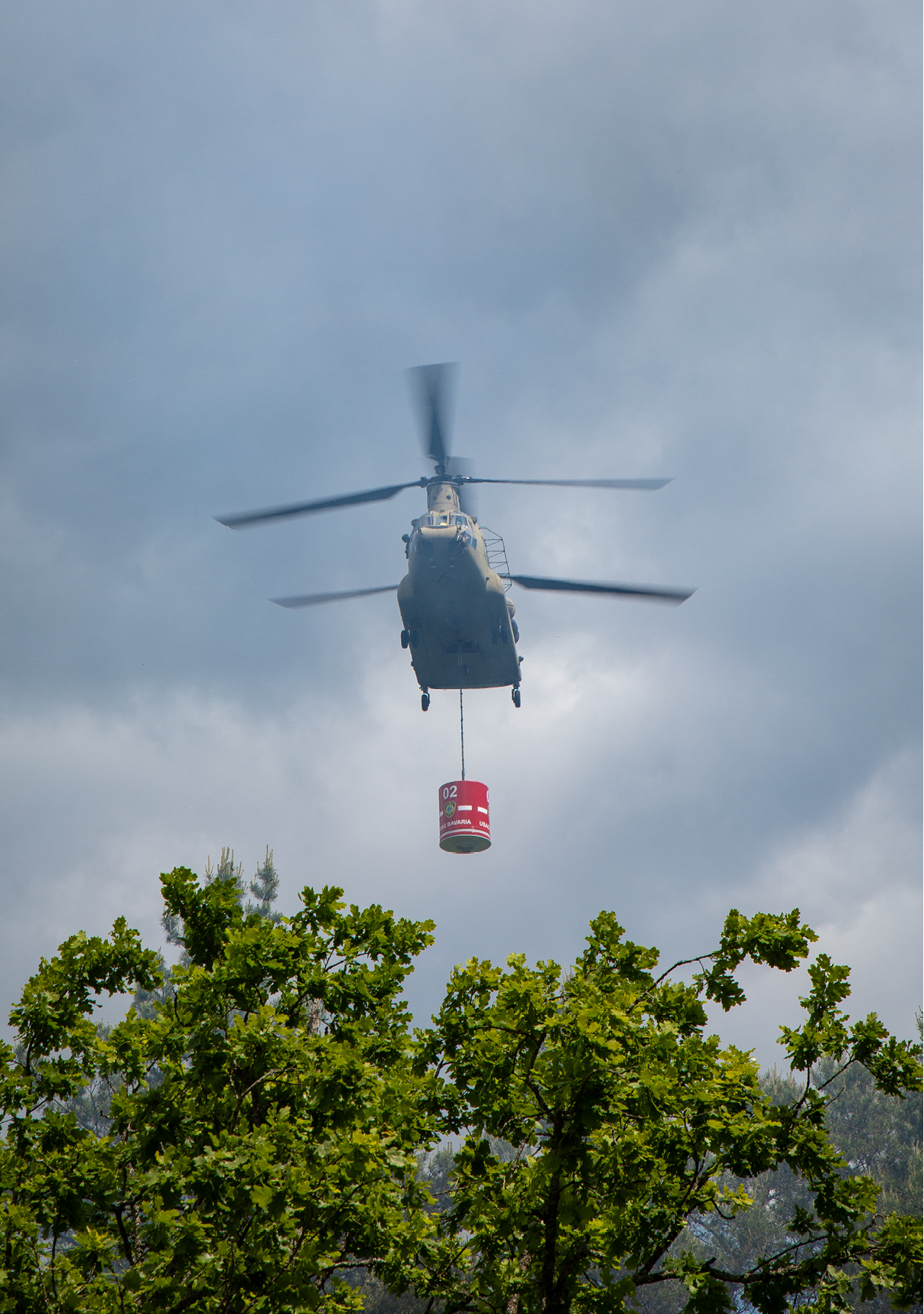 A helicopter is flying over a forest, carrying a red object. AI generated content