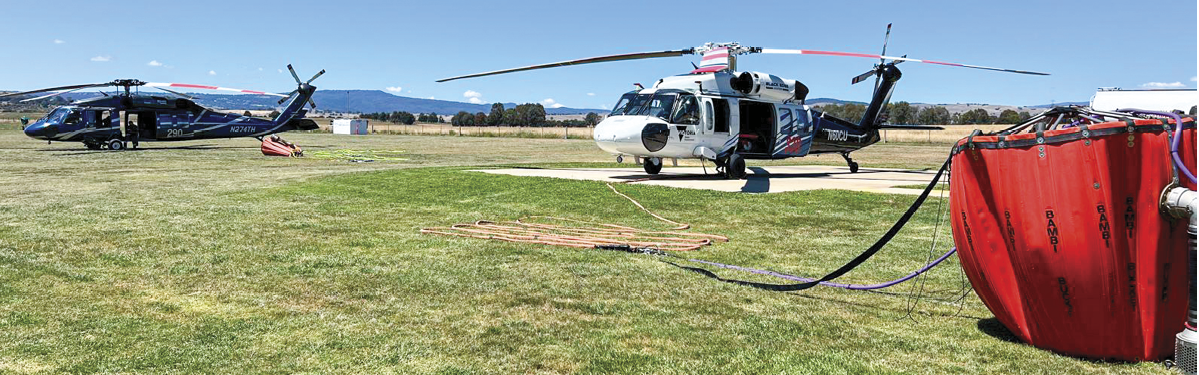 Two helicopters are parked on a grassy field. One helicopter is red and white, and the other is black and red. The red and white helicopter has a hose connected to it, possibly for refueling or maintenance. AI generated content