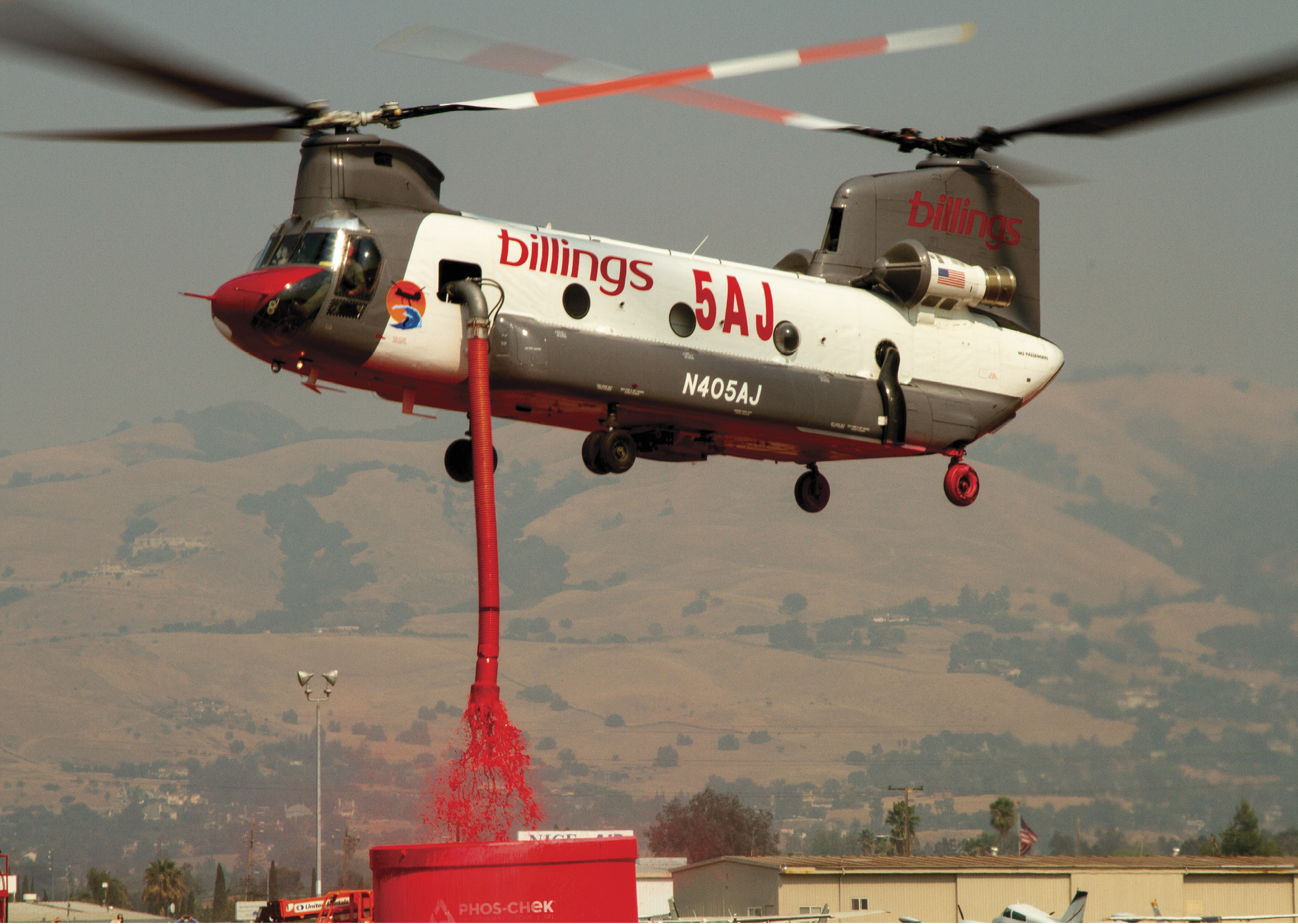 A red helicopter is flying over a red object, possibly a barrel, with a red substance pouring out of it. The helicopter is a military-style aircraft. AI generated content