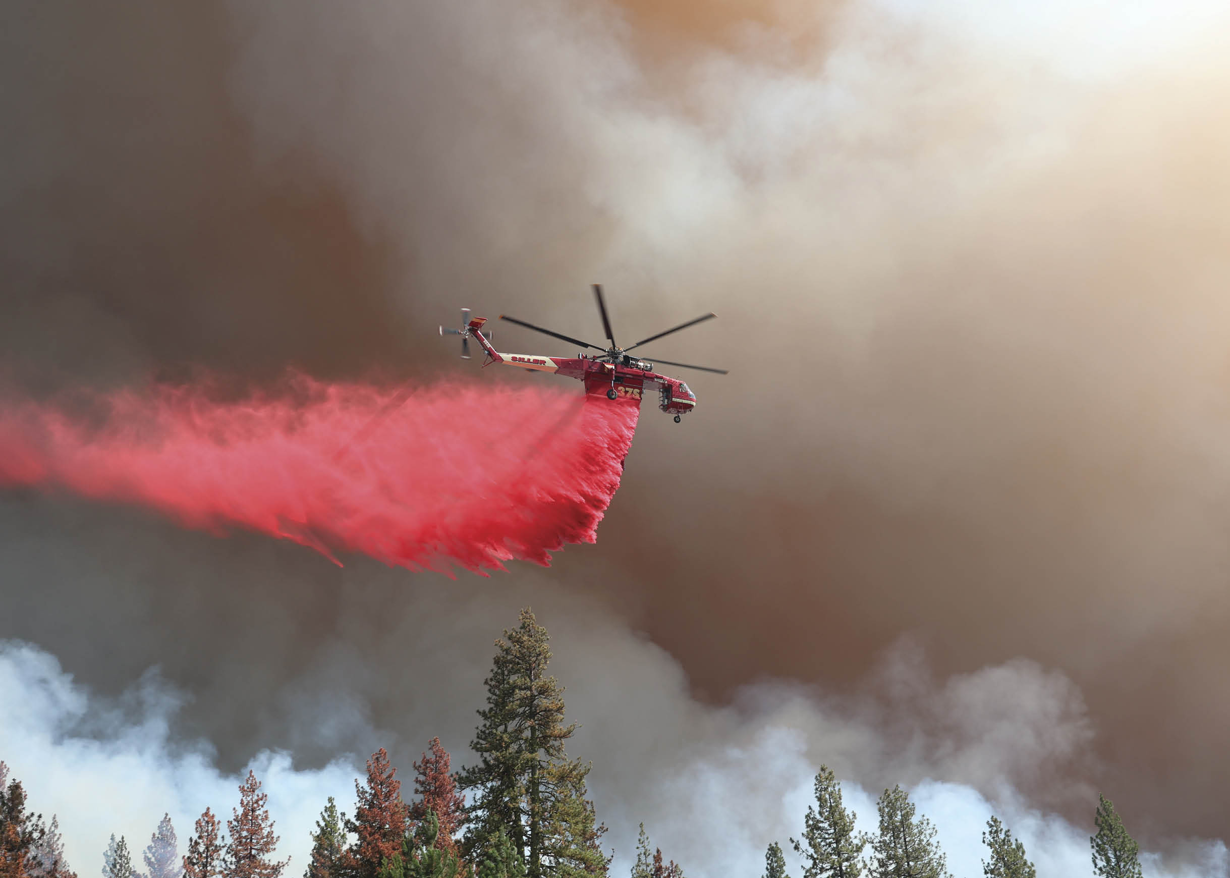 A red helicopter is flying through a cloud of smoke, possibly from a wildfire. AI generated content