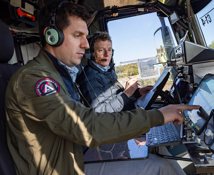 Two men in a vehicle, one of them operating a laptop. AI generated content