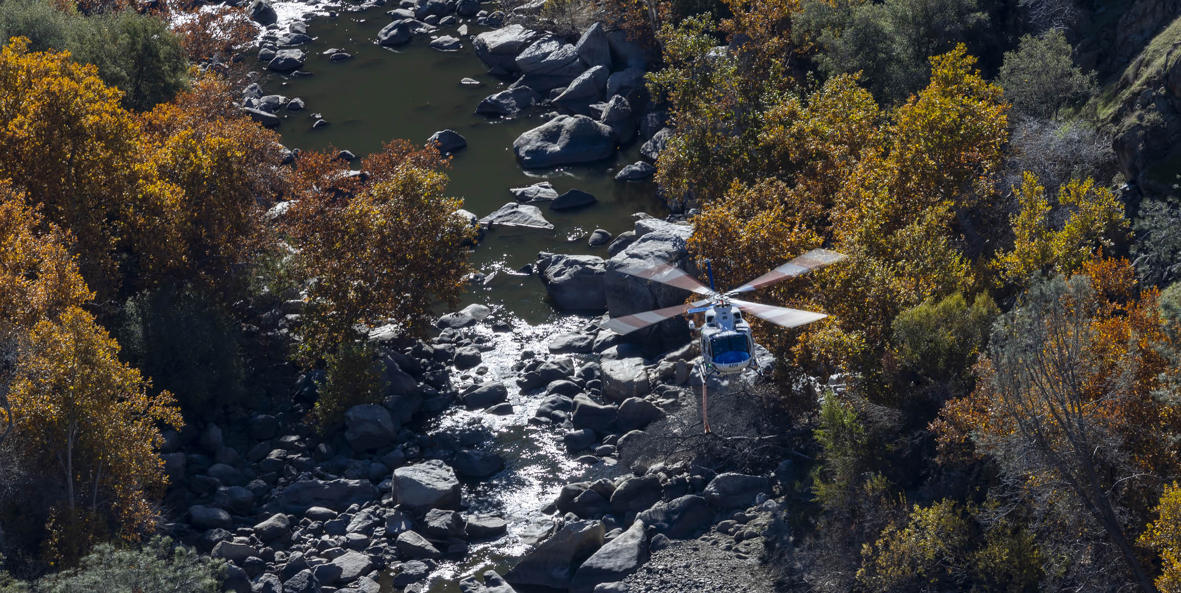 A helicopter is flying over a river with rocks and trees in the background. AI generated content