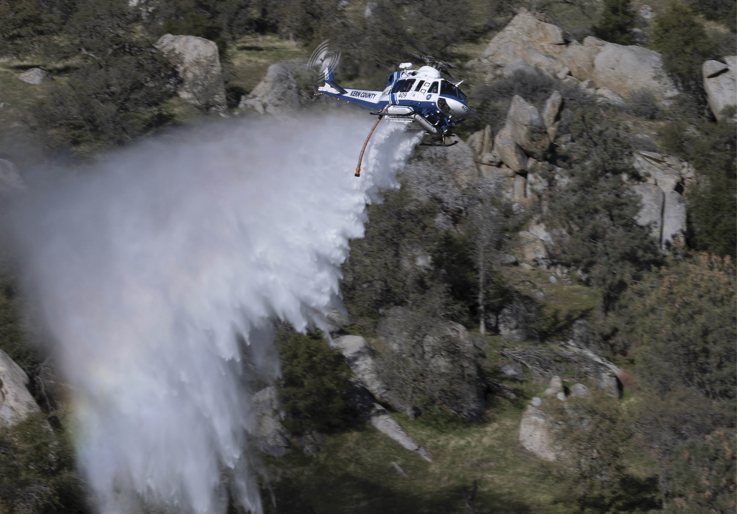 A blue and white helicopter is spraying water on a hillside. AI generated content