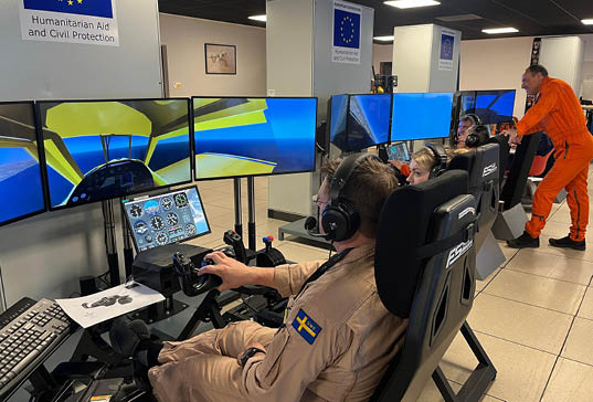 A man wearing a flight suit is sitting in a chair, using a computer and a joystick to control a flight simulation. AI generated content