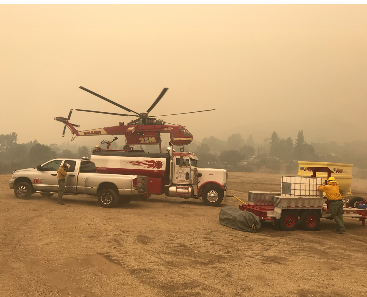 A red and white truck is parked on a dirt field with a helicopter on top of it. AI generated content