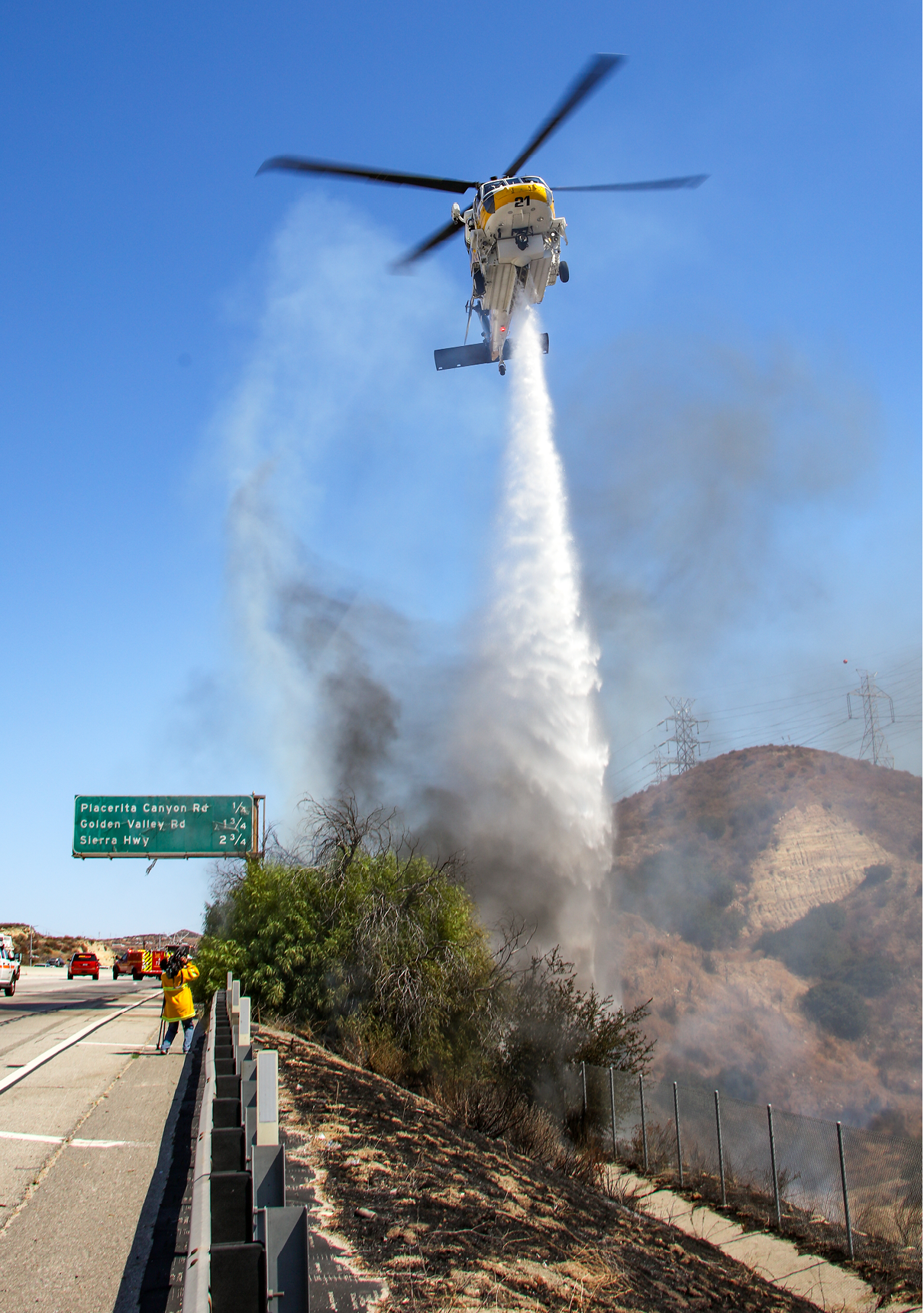 A helicopter is spraying water on a hillside, creating a firebreak. AI generated content