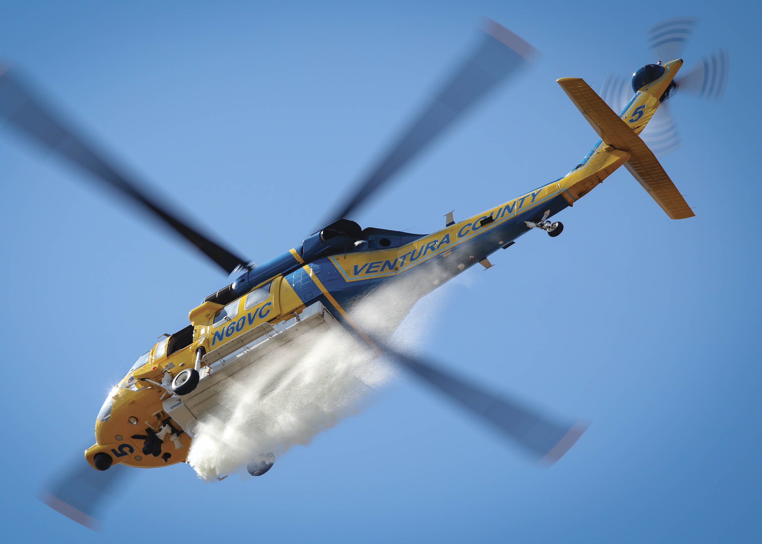 A yellow and blue helicopter is flying through the sky, leaving a trail of smoke behind it. AI generated content