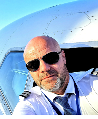 A man in a tan jacket stands in front of a yellow airplane. AI generated content