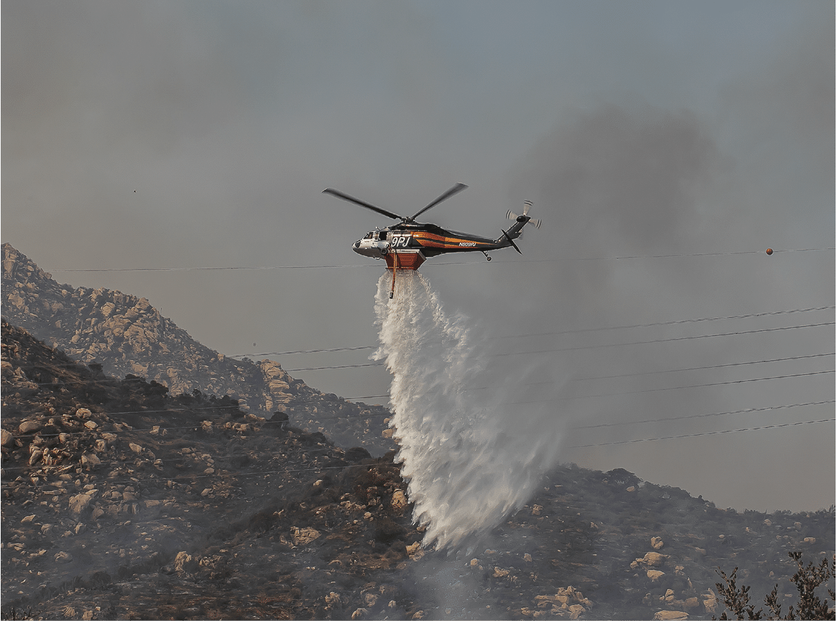 A helicopter is releasing water over a mountainous area, likely to extinguish a fire. Description generated by AI