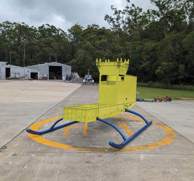 A small yellow model resembling a helicopter with a castle turret on top is placed on a concrete helipad outdoors near buildings and trees under a cloudy sky. Description generated by AI