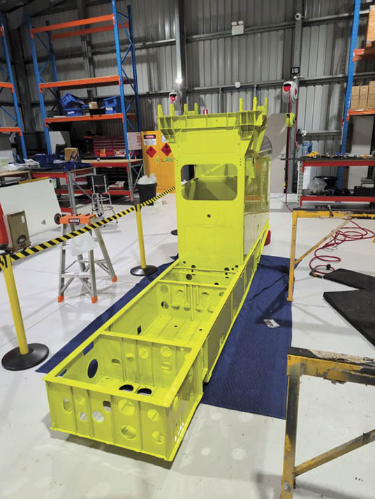 Several green plastic parts are arranged on a blue padded surface in a workshop setting with a wooden crate and cardboard box in the background. Description generated by AI