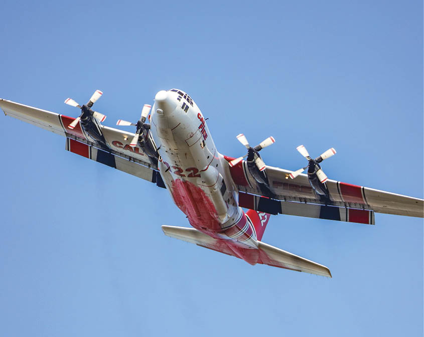 A red, white, and blue propeller airplane is flying against a clear blue sky, viewed from below. Description generated by AI