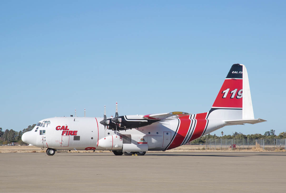A large white and red firefighting aircraft with “CAL FIRE" and the number "119" on its tail is parked on a runway under a clear blue sky. Description generated by AI