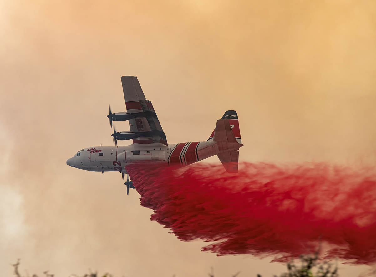 A firefighting airplane is releasing a large plume of red fire retardant over a smoky landscape. Description generated by AI