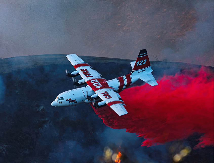 A firefighting airplane is releasing a large plume of red fire retardant over a smoky landscape. Description generated by AI