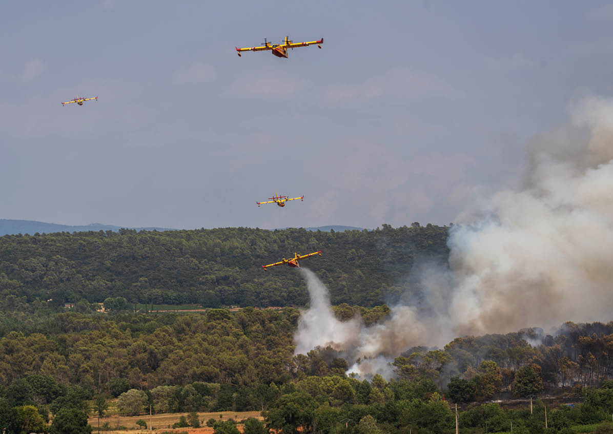 Several firefighting planes are flying over a forested area releasing water or fire retardant to combat a wildfire producing thick smoke. Description generated by AI