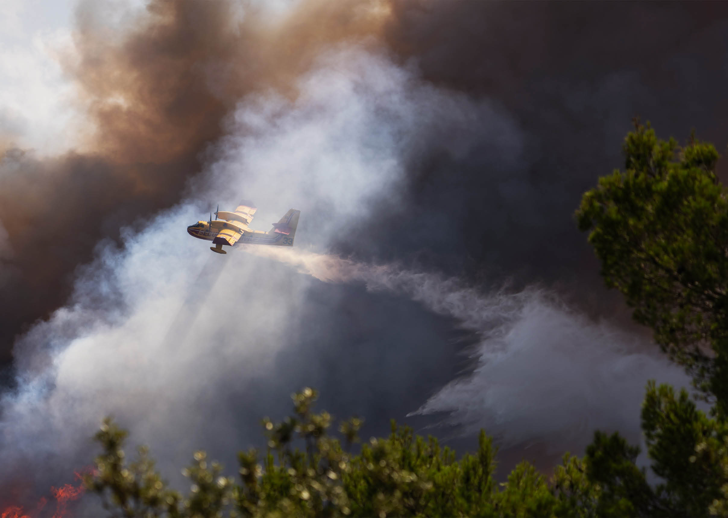 A firefighting plane is releasing water over a forest fire with thick smoke and flames visible among the trees. Description generated by AI