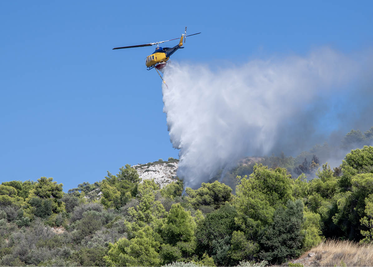 A helicopter is releasing a large spray of water over a forested area to extinguish a fire. Description generated by AI