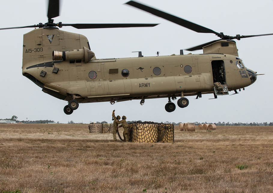 Lance Corporal Jesse Ablett and Private Matt Crabtree work together to hook a load of three round hay bales under an Australian Army CH-47 Chinook helicopter as it hovers above them as part of an animal feed drop at Bairnsdale airport, Victoria.