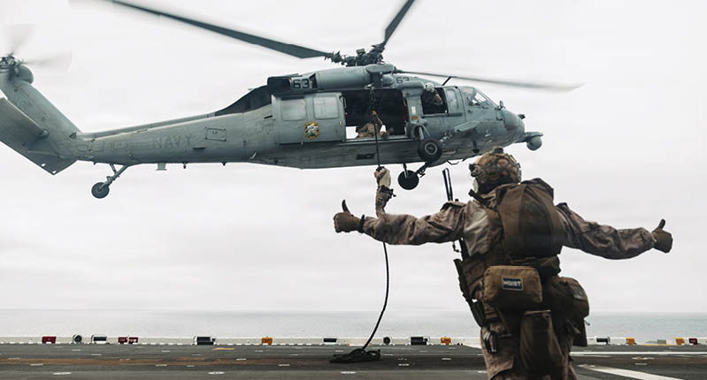 A man in a brown uniform is standing on a helicopter deck, waving at a helicopter that is flying above him. AI generated content