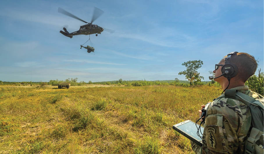 A man wearing a camouflage uniform is standing in a field, looking at a tablet computer. In the background, a helicopter is flying overhead. AI generated content