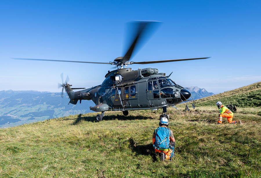 A helicopter is on a grassy hill, with a group of people standing nearby. AI generated content