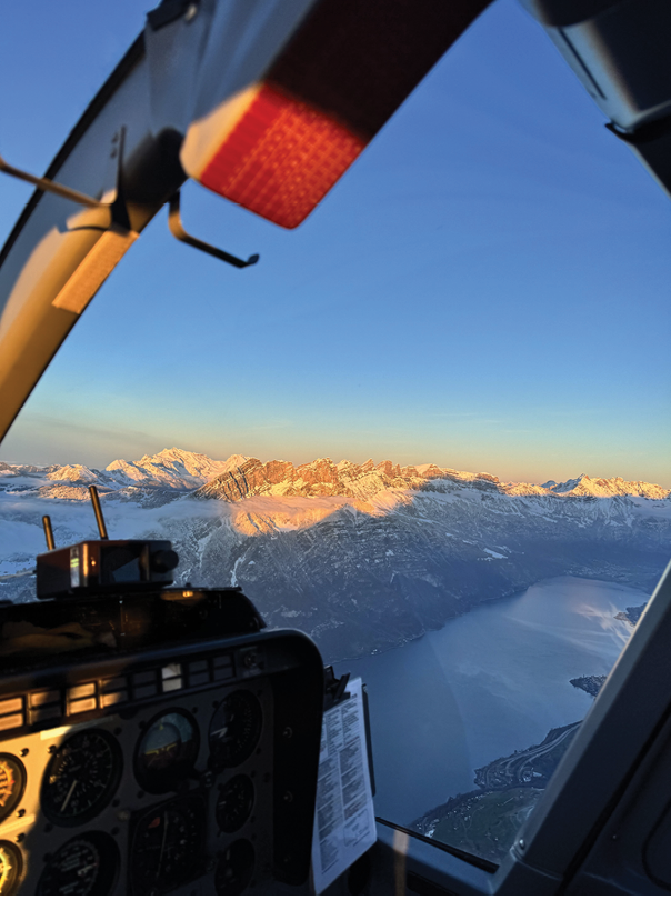 A cockpit of a helicopter with a view of mountains and a lake. AI generated content