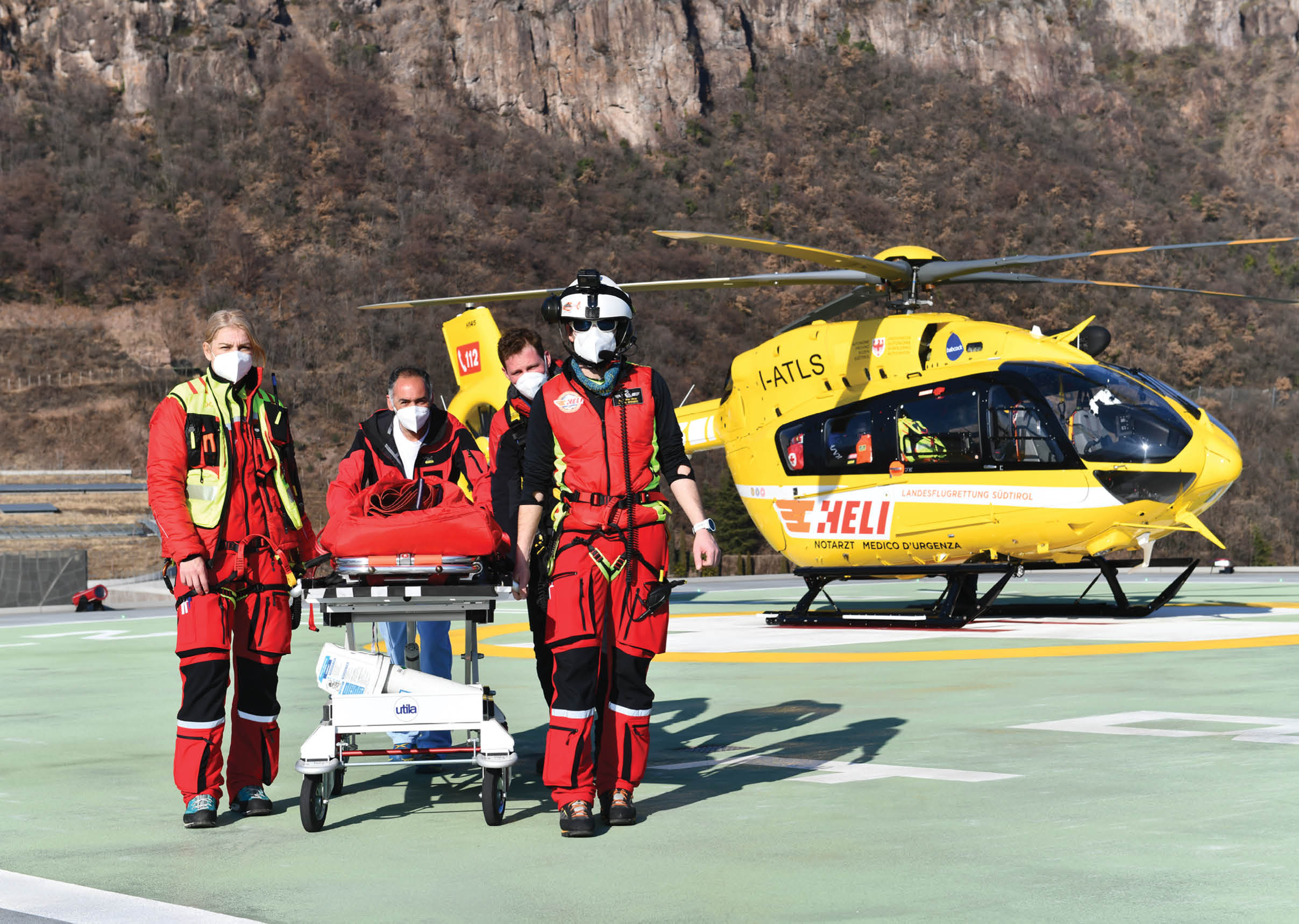 A yellow helicopter with a man in a red and black outfit standing next to it. Description generated by AI