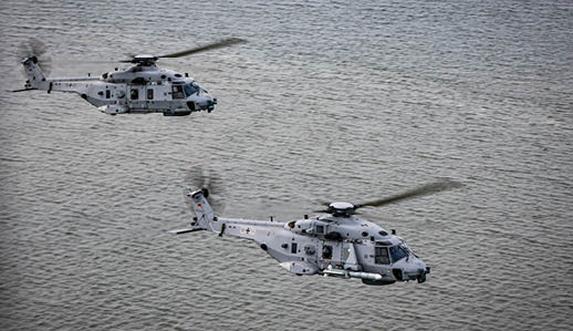 Two helicopters flying over water. Description generated by AI
