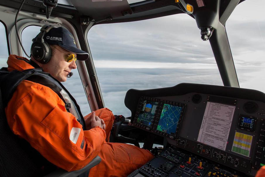 A man wearing a orange and black outfit is sitting in a cockpit of a helicopter. Description generated by AI