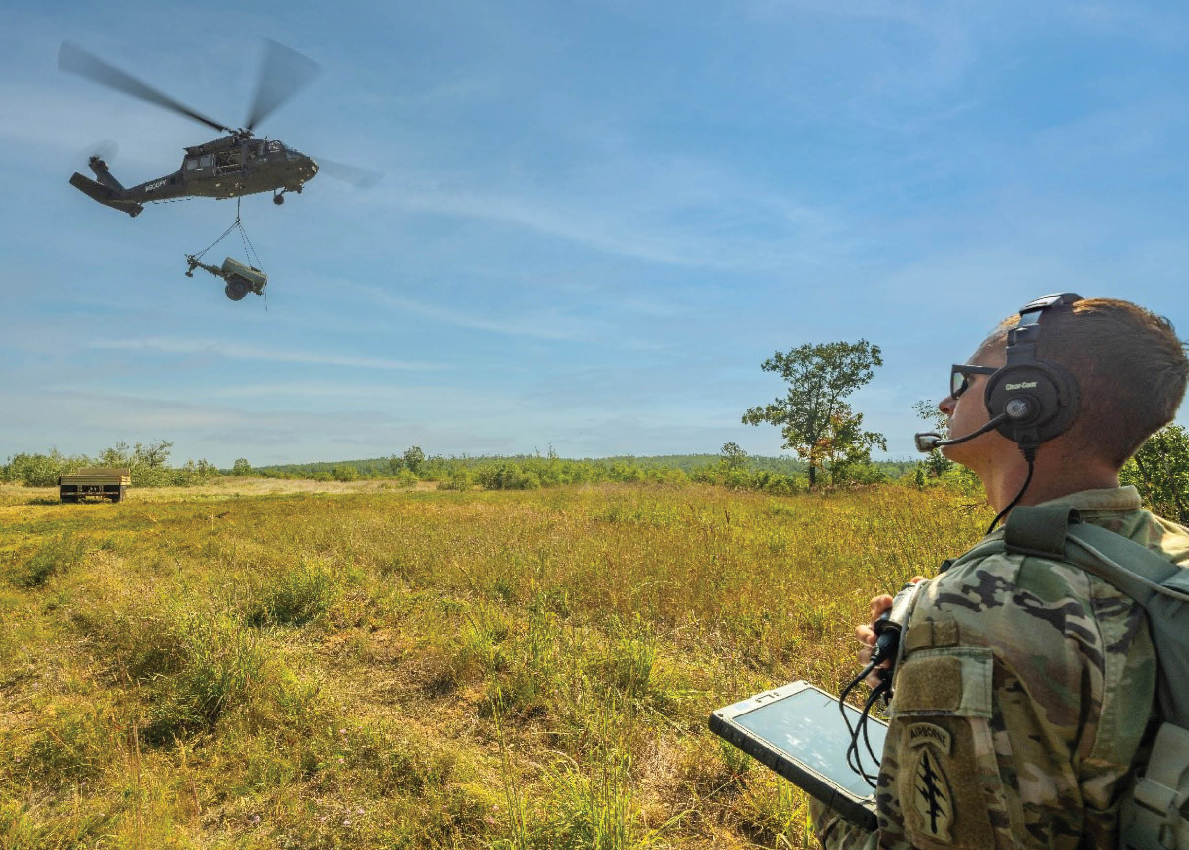 A man in a camouflage uniform is watching a helicopter fly by. Description generated by AI