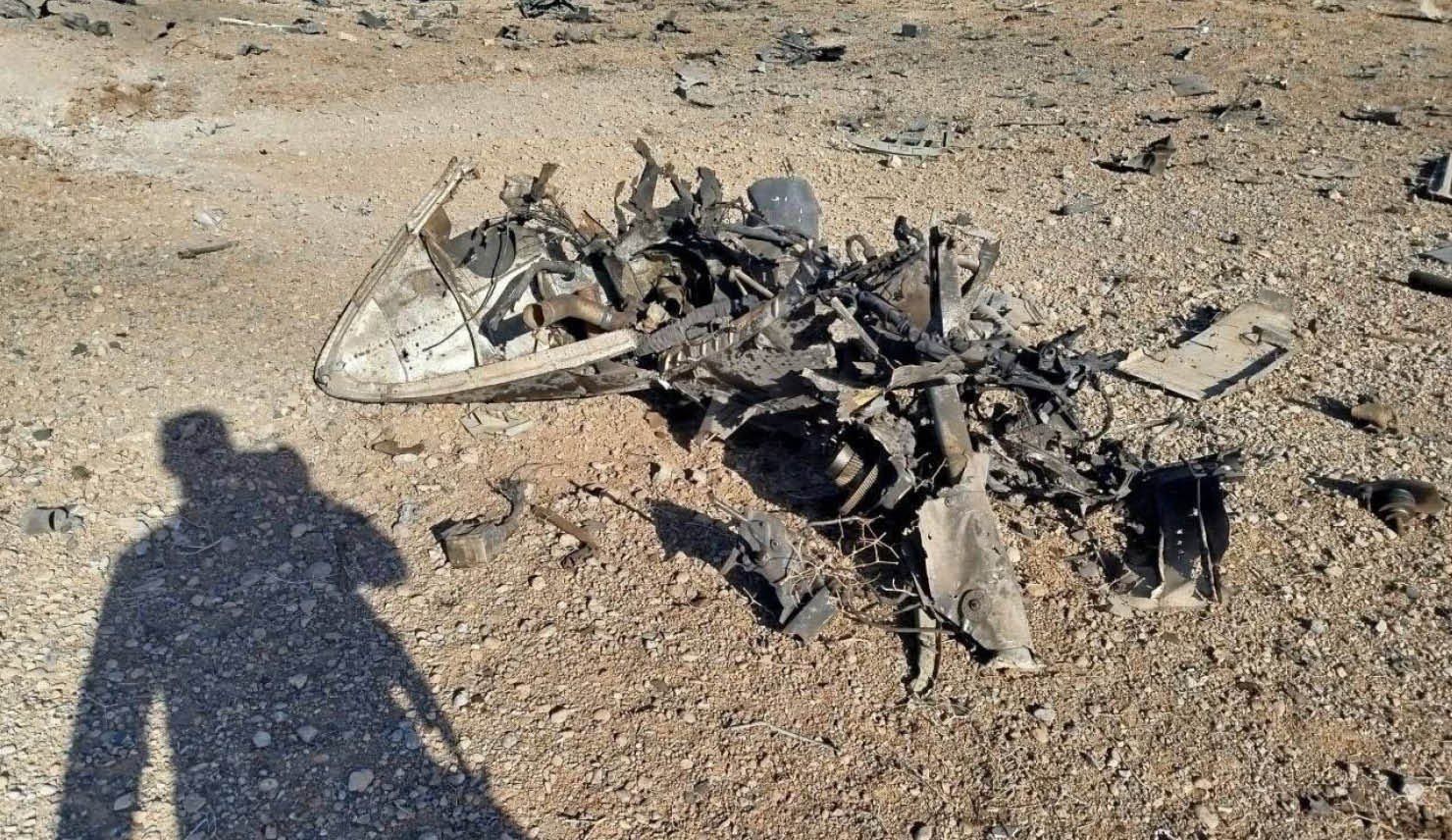 A shadow of a person is on the ground next to a broken airplane. Description generated by AI