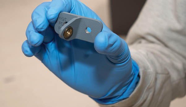 A person wearing blue gloves is holding a metal piece. Description generated by AI