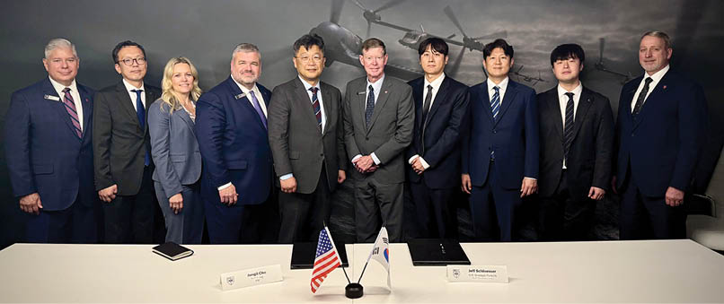 A group of people standing in front of a table with an American flag and a helicopter in the background. Description generated by AI