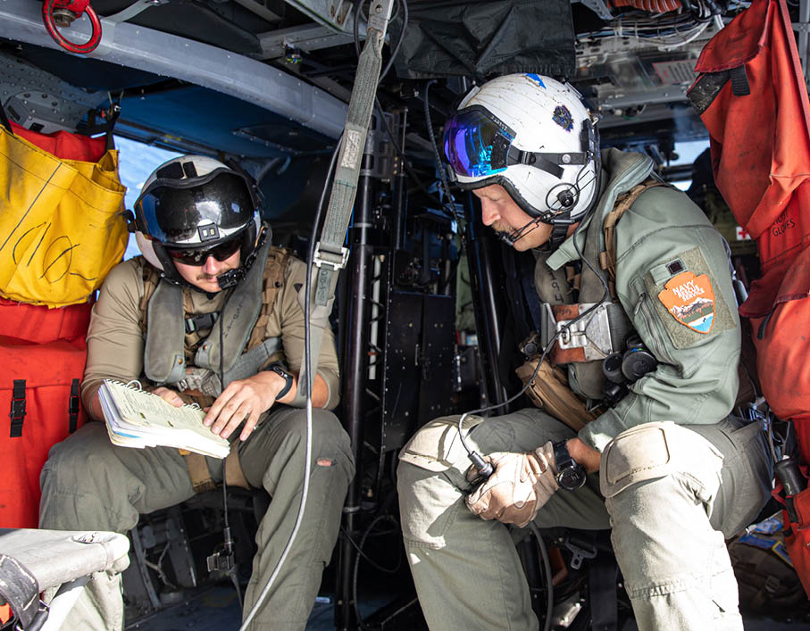 A man in an orange and black suit is being lifted out of a helicopter. Description generated by AI